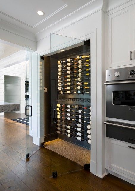 Glass-walled wine room with wall-mounted racks beside white kitchen cabinetry